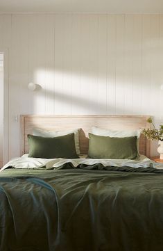 a bed with green sheets and pillows in a white room next to a wooden headboard