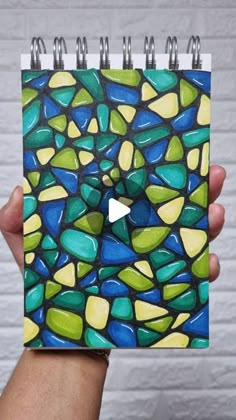 a hand holding up a spiral notebook with stained glass on it