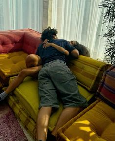 two people laying on top of a yellow couch