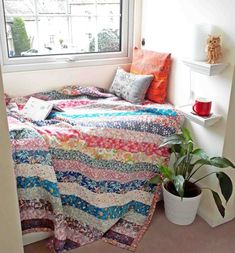 a bed with a colorful quilt on it next to a potted plant in front of a window