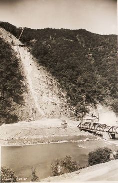 an old black and white photo of a bridge over a river in front of a mountain