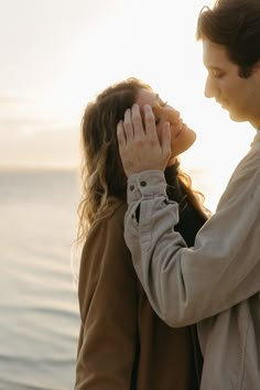 a man and woman standing next to each other near the ocean with their hands together