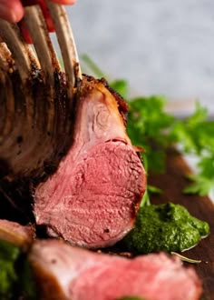 someone is cutting up some meat with chopsticks on a wooden board and green vegetables