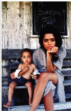 a woman sitting on top of a wooden bench next to a baby