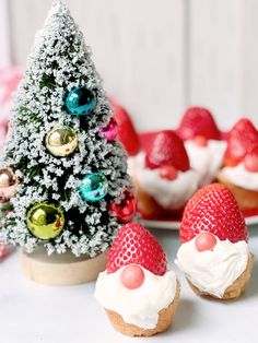 some cupcakes with frosting and strawberries on them next to a small christmas tree