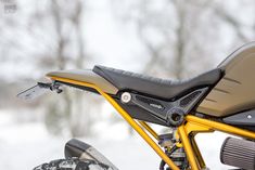 the front end of a yellow and black motorcycle in the snow with trees in the background