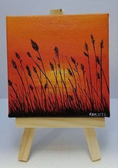 an easel with a painting on it that has grass in the foreground and sunset in the background