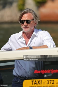 an older man in white shirt and sunglasses leaning out the window of a taxi car