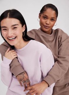 two women standing next to each other with tattoos on their arms and hands, both smiling at the camera