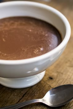 a white bowl filled with chocolate on top of a wooden table next to a spoon