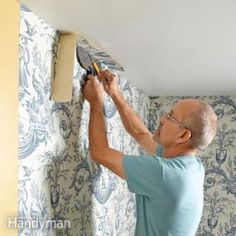 an older man is painting the walls in his living room with blue and white wallpaper