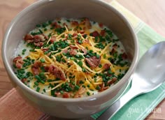 a bowl of soup with bacon, cheese and chives on a green place mat