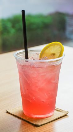 a drink with a lemon wedge on the rim and a black straw in it sitting on a wooden table