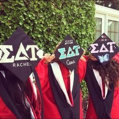 three graduates in caps and gowns hold up their hats with the word tat on them