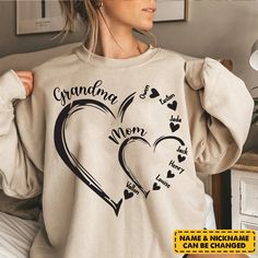 a woman wearing a sweatshirt with the words grandma and heart in black ink on it