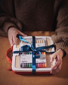 a person is holding an art box with colored crayons