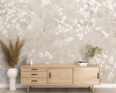 a white vase sitting on top of a wooden dresser next to a wall with flowers