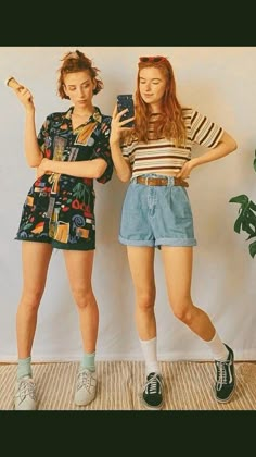 two young women standing next to each other in front of a white wall holding cell phones