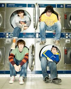 three young men sitting in front of washing machines