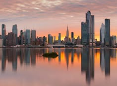 a city skyline is reflected in the water at sunset, with skyscrapers and other tall buildings