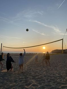 people playing volleyball on the beach at sunset