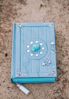 a blue book sitting on top of a sandy beach next to a white stick and bottle