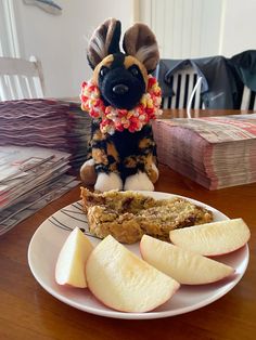 a stuffed animal sitting on top of a white plate next to sliced apples and bread