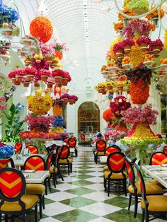 the inside of a restaurant with lots of tables and chairs covered in colorful flowers hanging from the ceiling