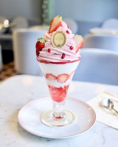 a dessert with strawberries and whipped cream in a glass on a white saucer