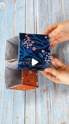 two hands are holding an origami box on a wooden table with blue and orange designs