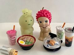 an assortment of food and drink items on a white tablecloth with two plastic dolls