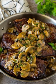 a pan filled with meat covered in mushrooms and garnished with parsley on the side