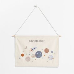 a white wall hanging with an image of the planets and stars on it, that says christopher