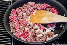 meat and onions cooking in a skillet on the stove with a wooden spatula