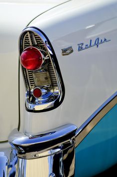 the tail end of an old car that is white with blue trim and chrome accents