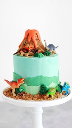 there is a cake that has dinosaurs on it and sand in the bottom tiers