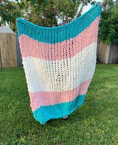 a crocheted blanket sitting on top of a green grass covered field next to a fence