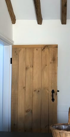 a wooden door in a white room with exposed beams on the ceiling and a basket next to it