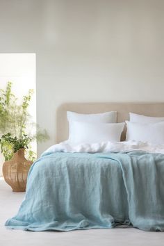 a bed with white sheets and pillows in a room next to a potted plant