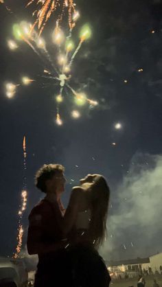 two people standing next to each other with fireworks in the sky