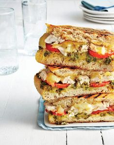 a stack of four sandwiches sitting on top of a white table next to plates and glasses