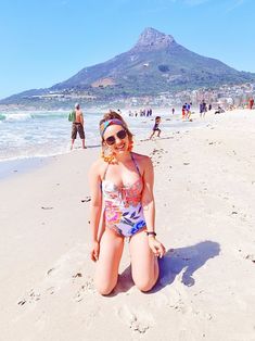 a woman is sitting on the beach in her bathing suit and headband, smiling at the camera