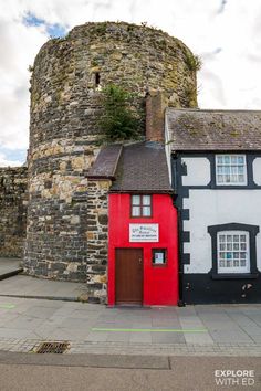 a red and white house next to a brick wall with a tower on top in the background