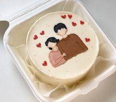 there is a cake in the box with two people on it and hearts all around