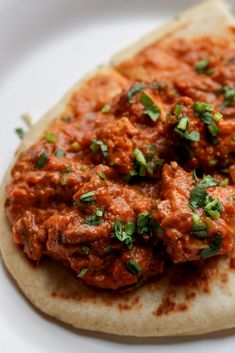 a tortilla topped with meat and garnish on top of a white plate