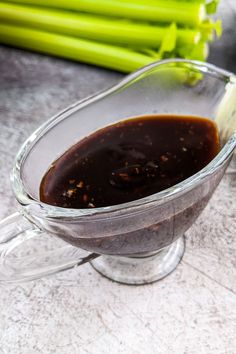 a glass gravy dish filled with sauce next to celery stalks on a table