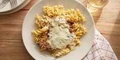 a white plate topped with pasta covered in gravy next to a glass of wine