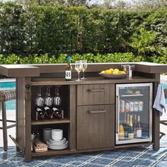 an outdoor bar with wine glasses and bottles on it next to a swimming pool, surrounded by wicker chairs