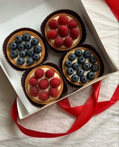 four cupcakes in a box with berries and blueberries on top, tied to a red ribbon