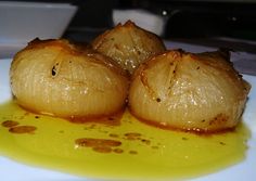 three onions sitting on top of a white plate covered in oil and brown substance next to a bowl